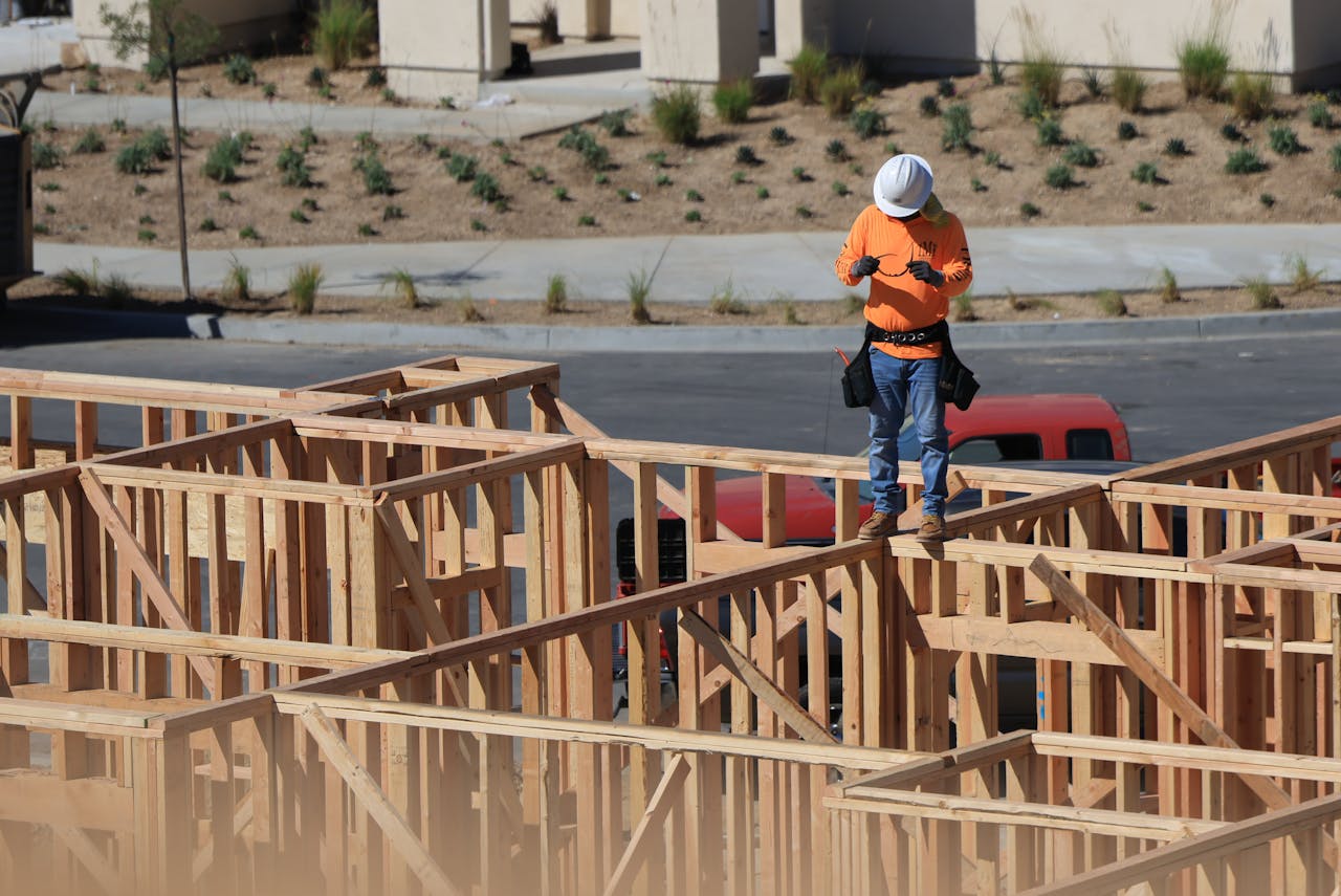 About A construction worker on a wooden frame checks a device at a building site.