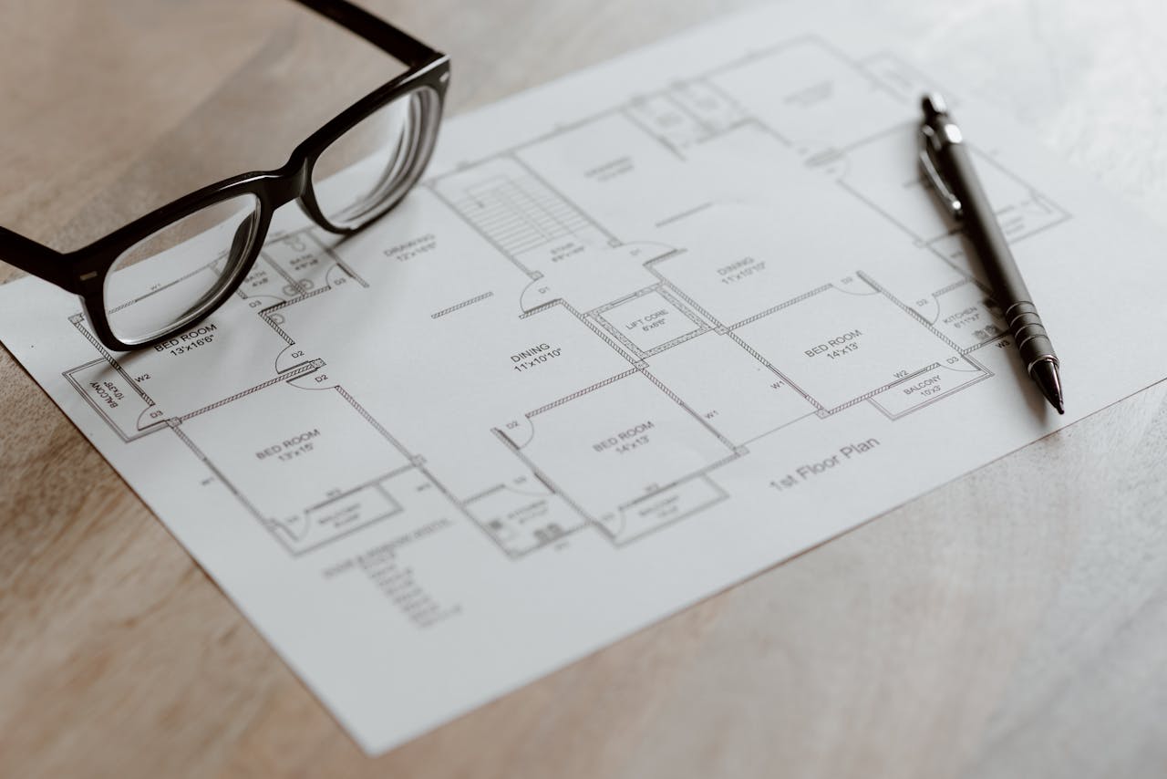 Services Composition of plan of room and black pen with eyeglasses placed on wooden table at daytime