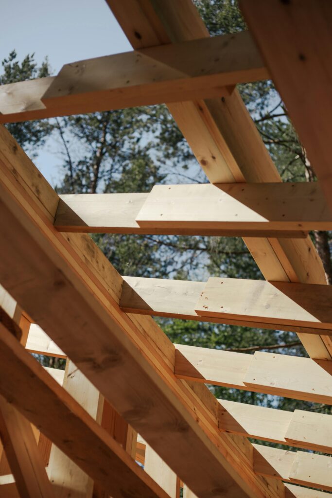 pexels photo 8817839 8817839 Close-up view of wooden beams forming a house roof structure against a sky background.